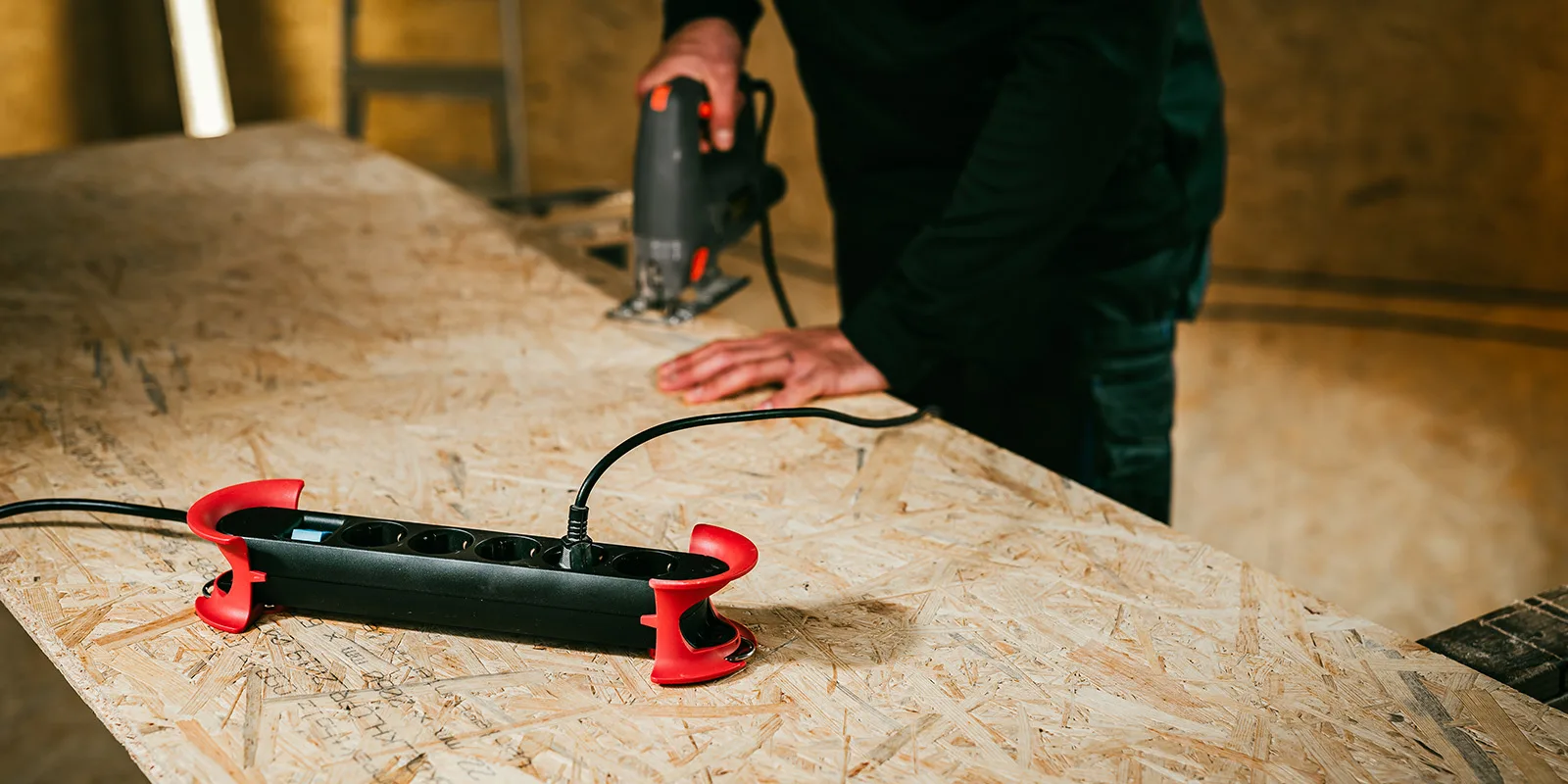 A black power strip with red mounts on a workbench while a carpenter saws