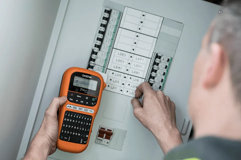 Electrician labels breakers in a panel with a Brother PT E110 label printer in hand