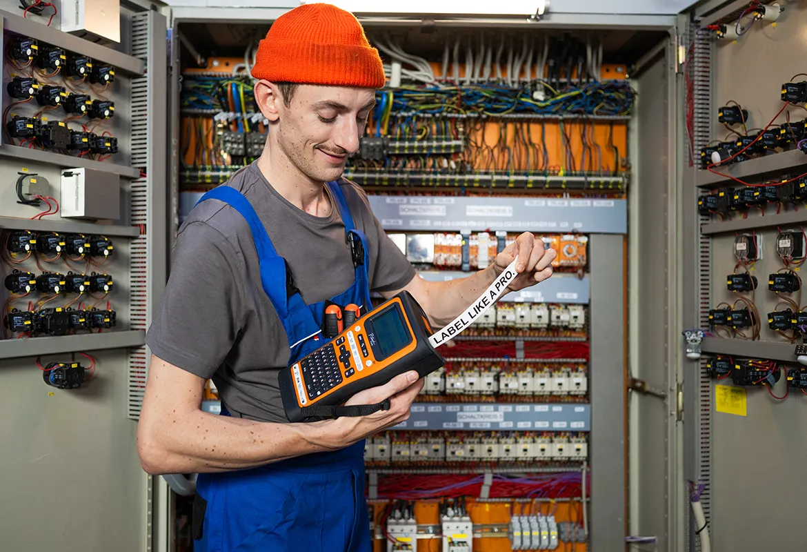 Electrician prints a label on a Brother label printer beside an open distribution board