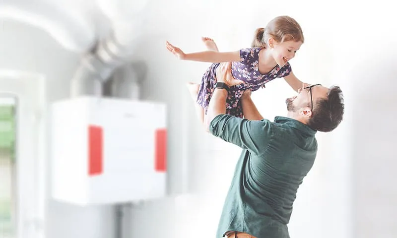 A father lifts his daughter up by a Helios ventilation system on the wall