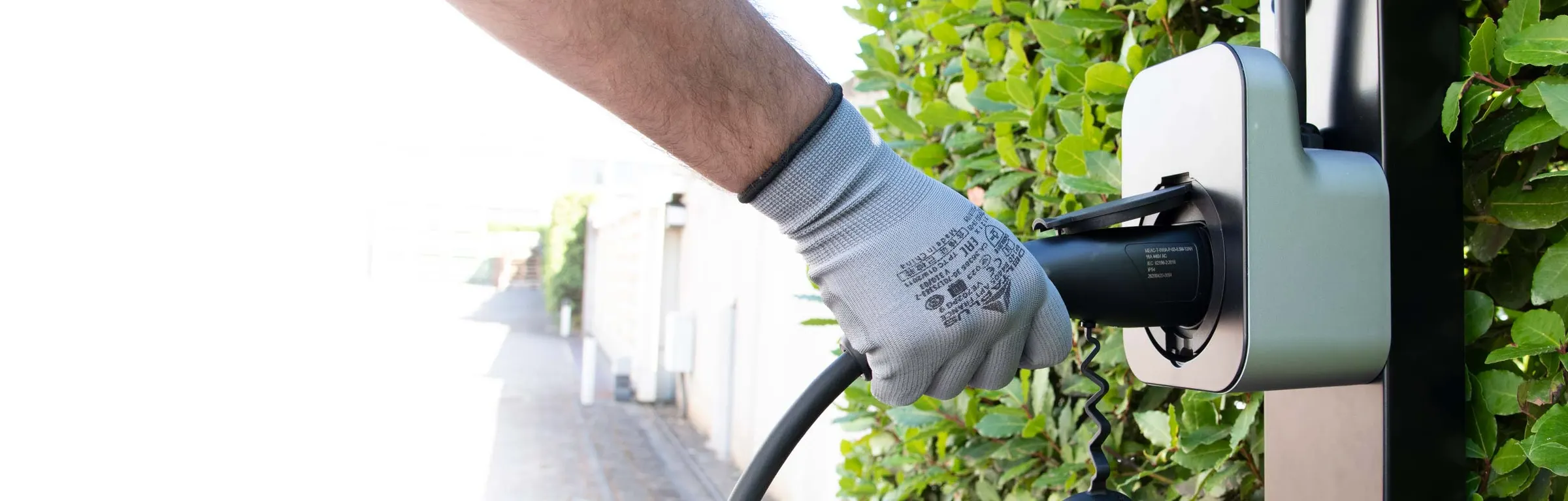 A hand plugs the test clamp of an HT adapter into a wall charging station
