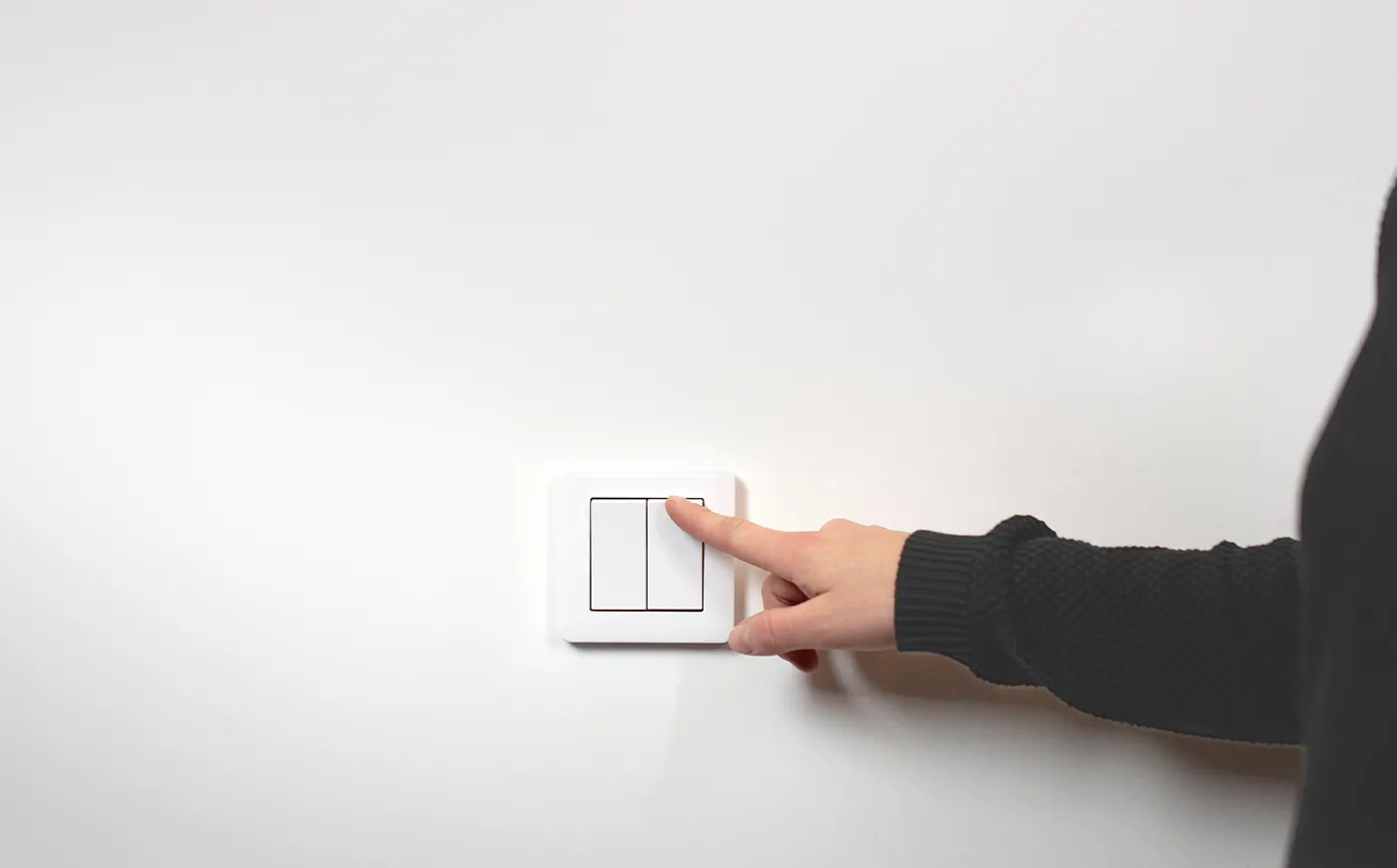 A hand presses an ordinary switch on a white wall
