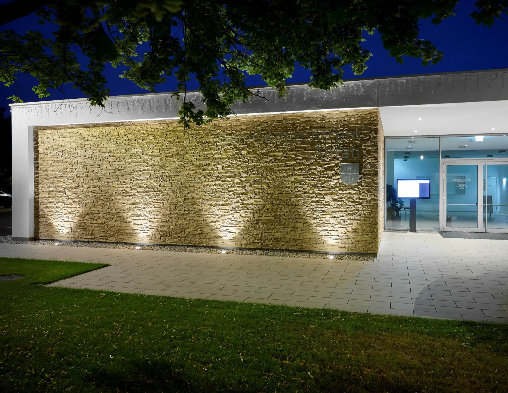 Lit stone wall by an entrance at night, in ground lights washing it with light