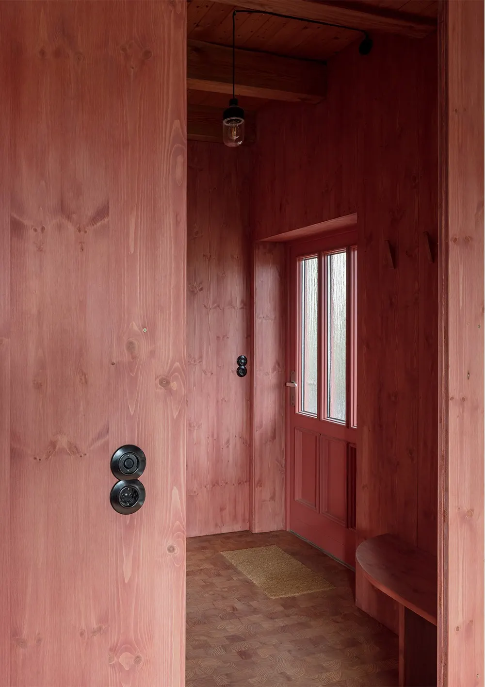 Hallway clad in red painted wood, two black Bakelite switches one above the other by the door