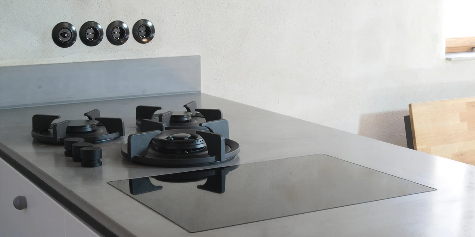 Concrete kitchen counter with gas burners and four black switches and sockets in a row