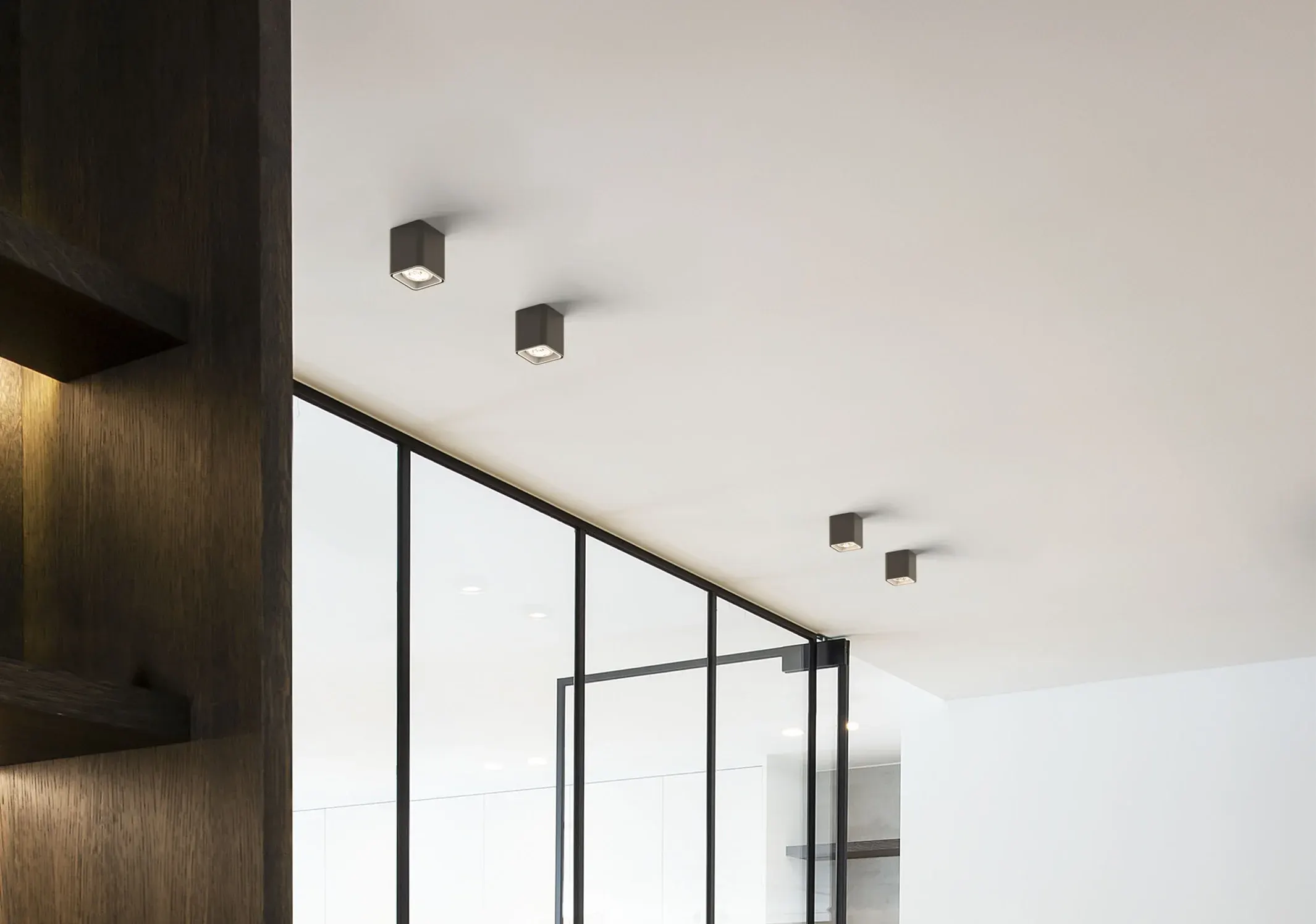 Square spotlights in a white ceiling beside a glass wall