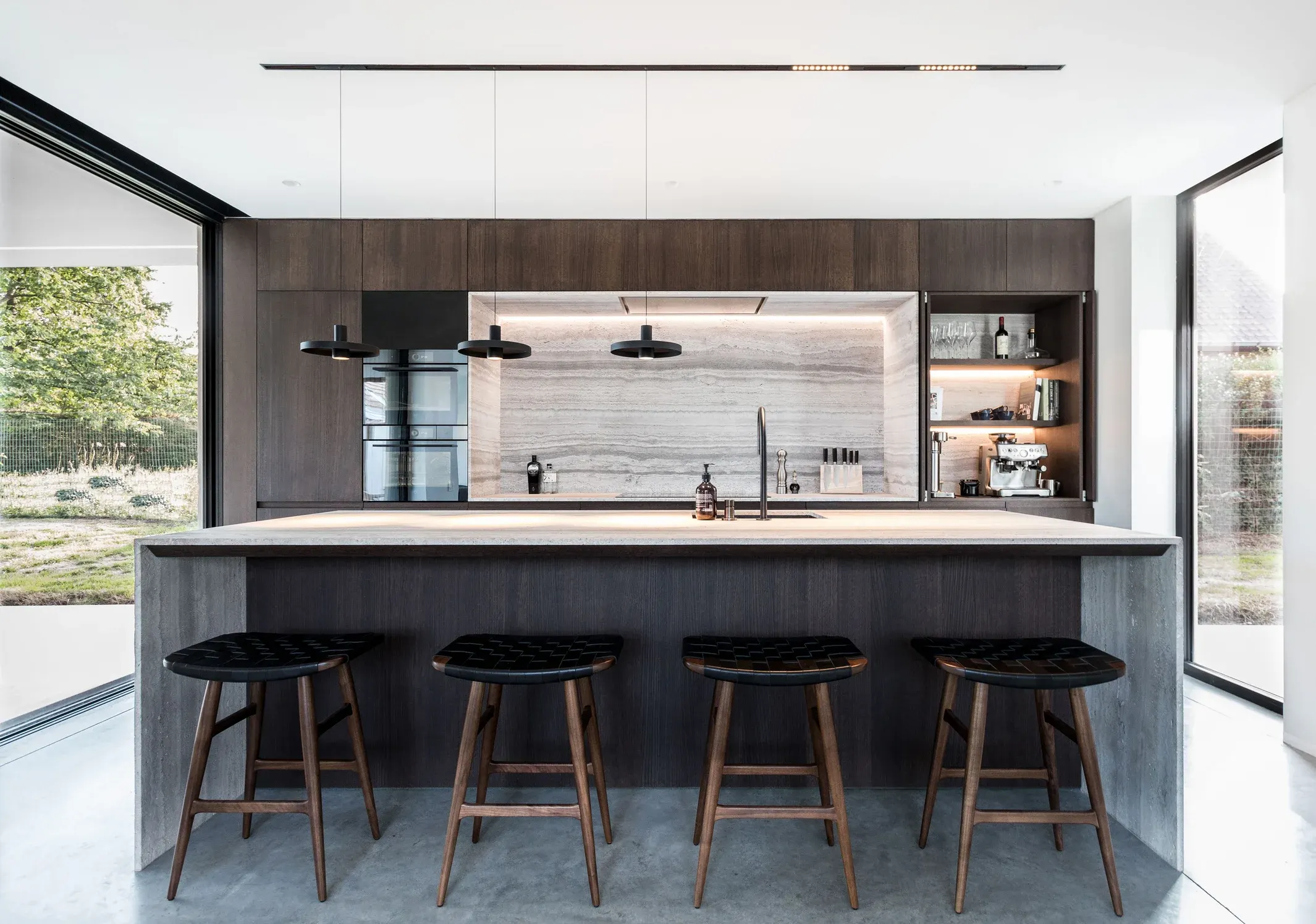 A kitchen with dark cabinetry, an island with four stools and pendant lights above