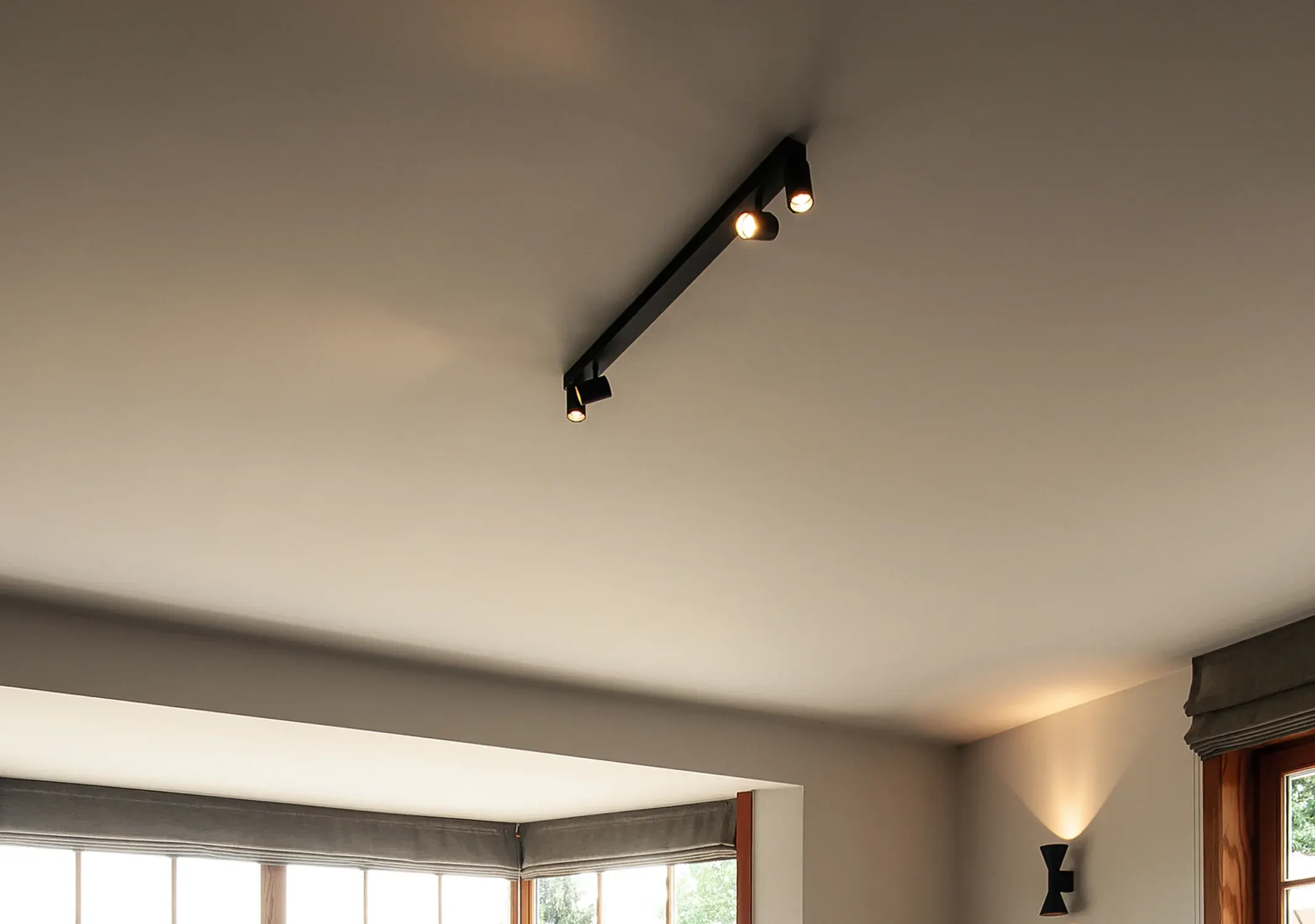 A black track with three spotlights in a living room ceiling and a wall light shining up and down