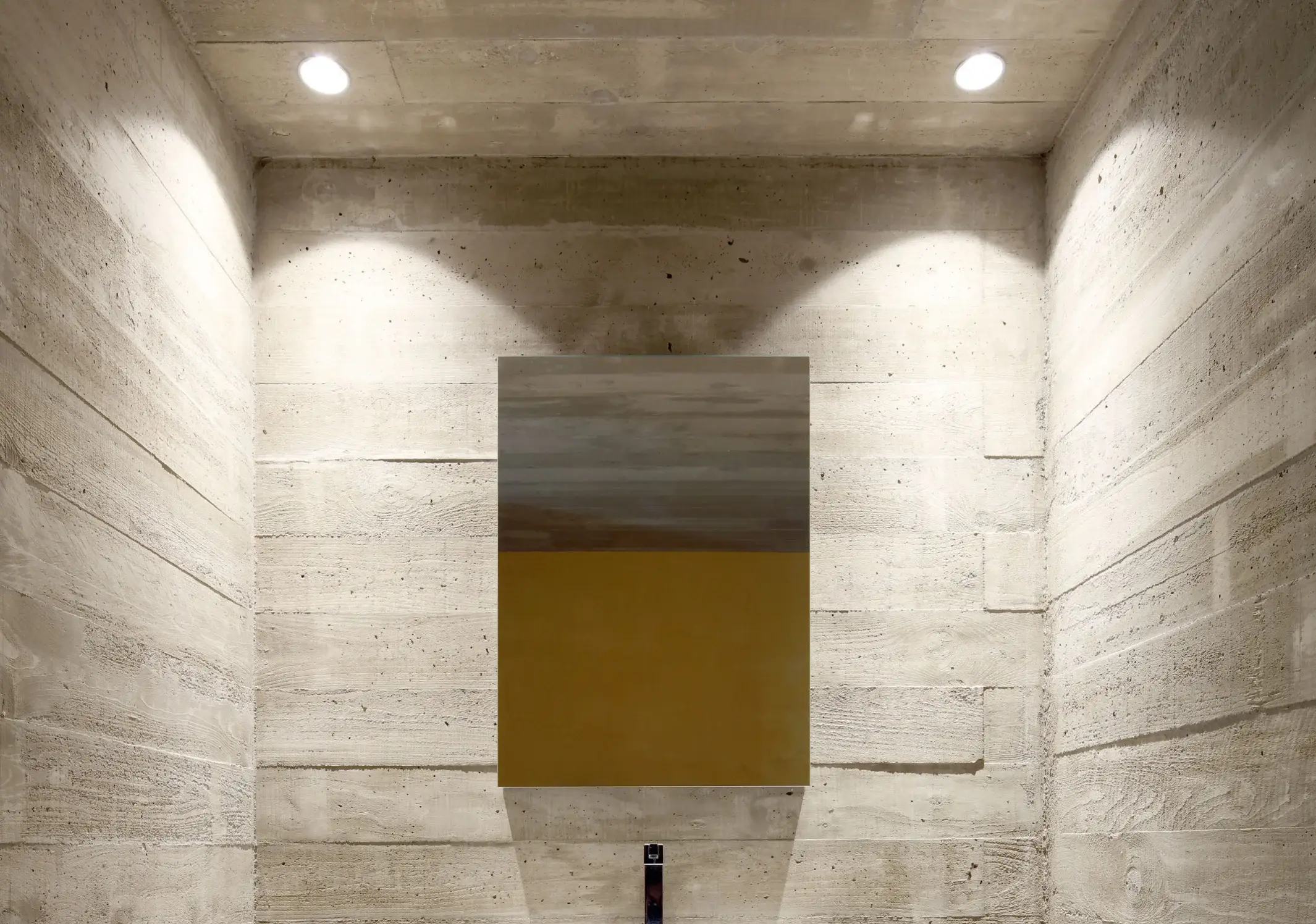 A concrete wall with a painting, lit by two recessed lights