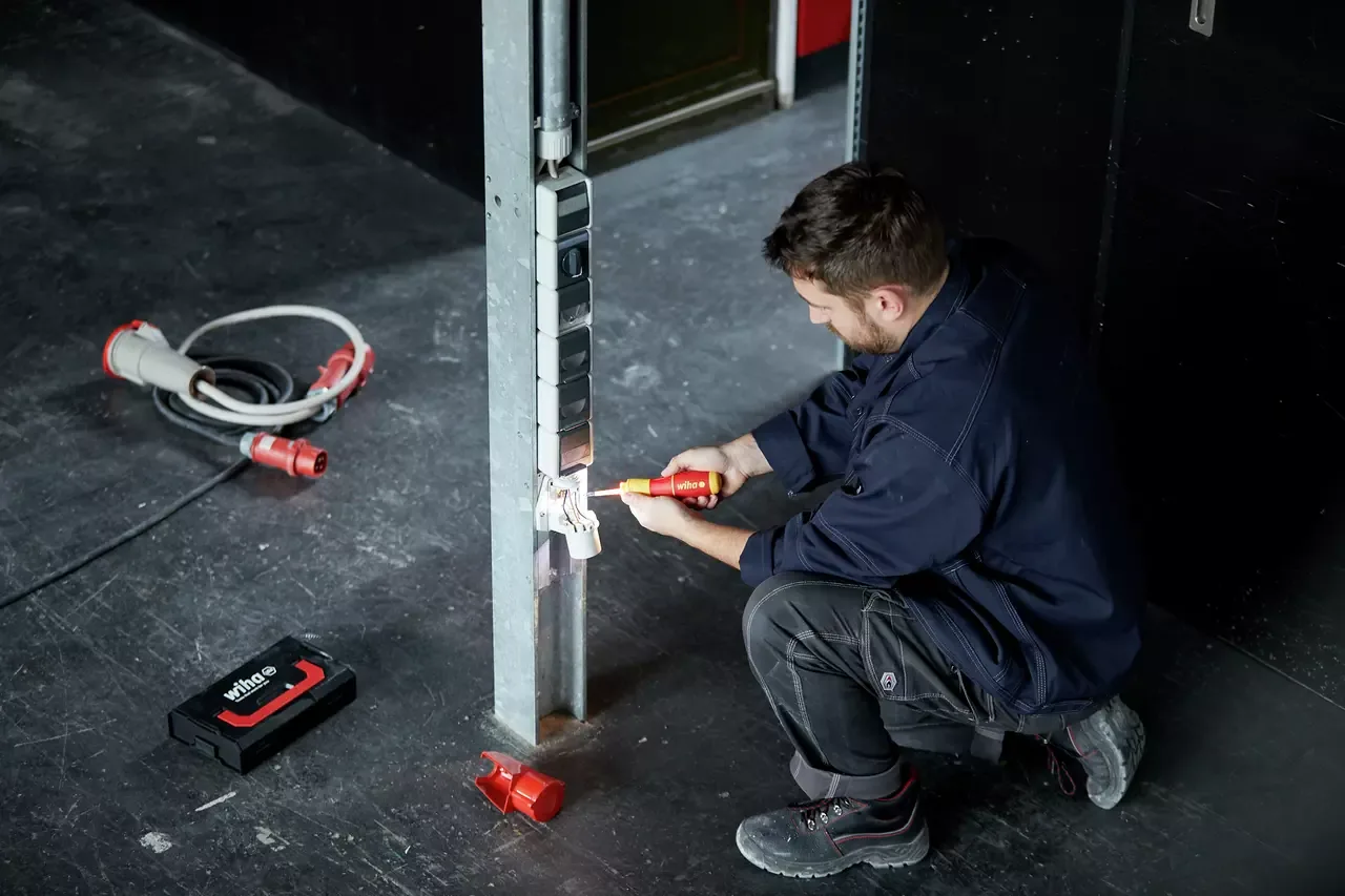 An electrician tightens a socket onto a socket column with an insulated Wiha screwdriver